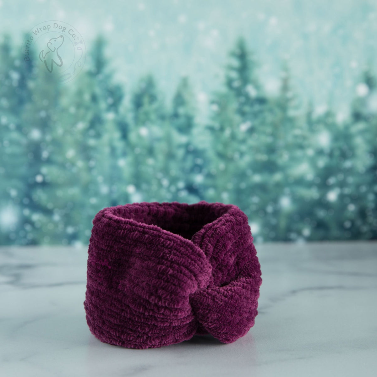 Deep mulberry chenille dog neckwarmer displayed against a snowy winter forest backdrop.