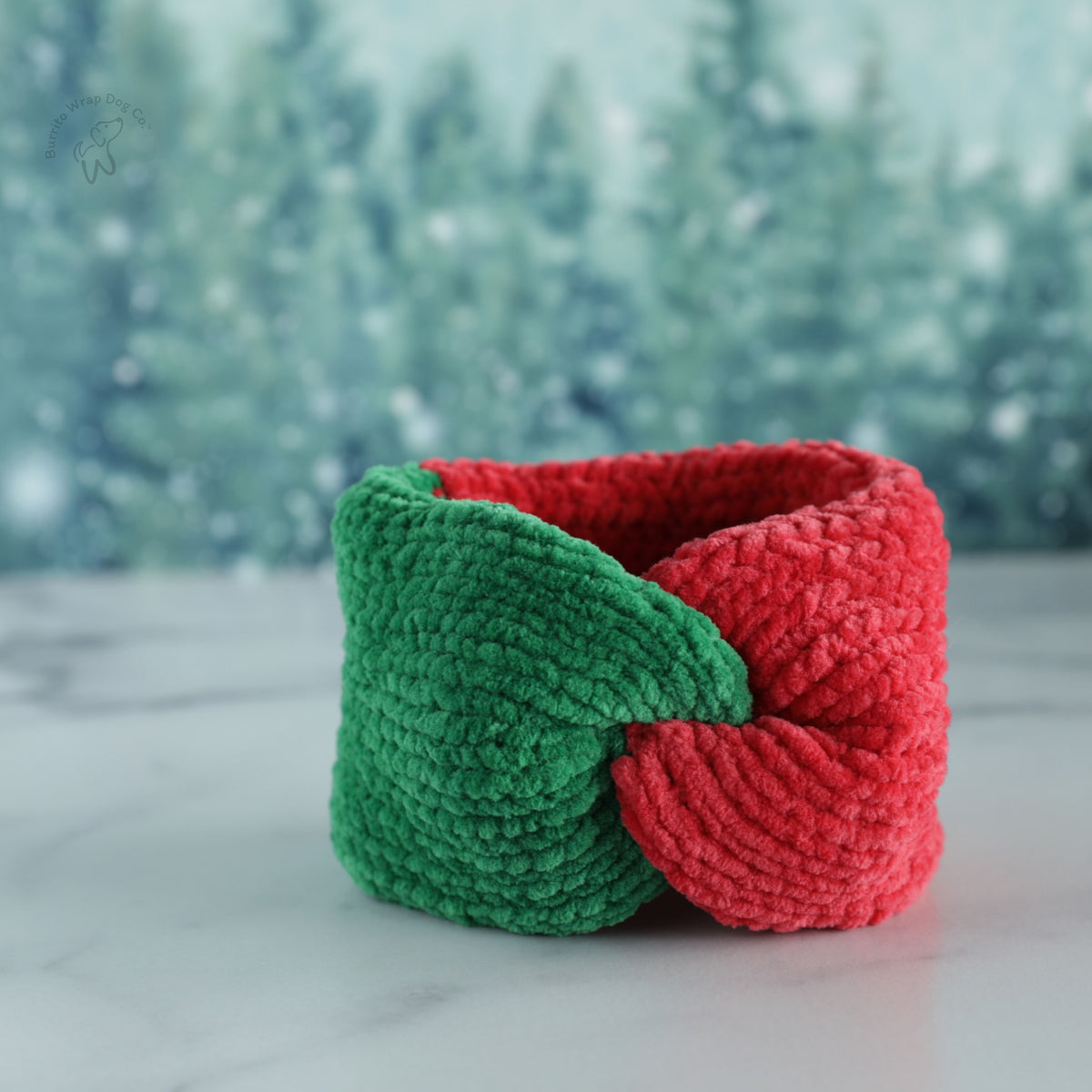 Red and green chenille dog neckwarmer displayed against a snowy winter forest backdrop.
